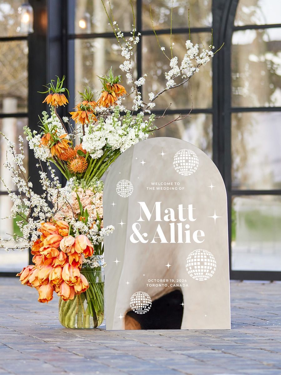 Arched mirror acrylic wedding welcome sign with white lettering, shown from side angle.